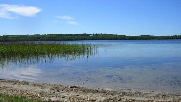 A calm lake with a distant hill and a small building.