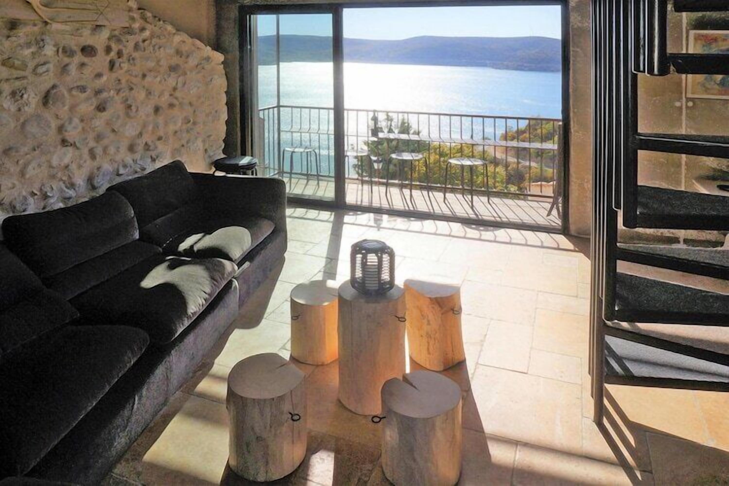 Ein modernes Wohnzimmer mit einer schwarzen Couch, einer Steinwand und Meerblick durch große Glasfenster.