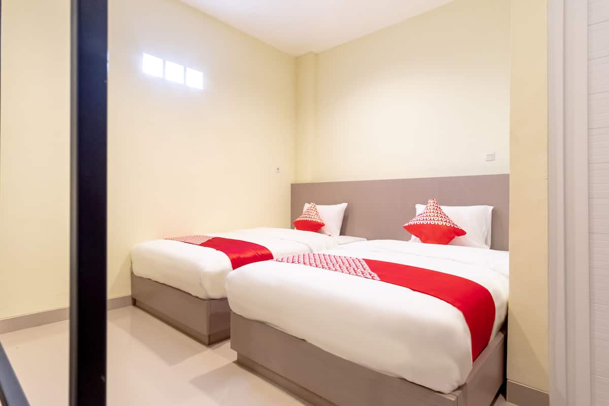 A hotel room with two beds, each with white bedding and red accents, and a neutral-colored headboard.