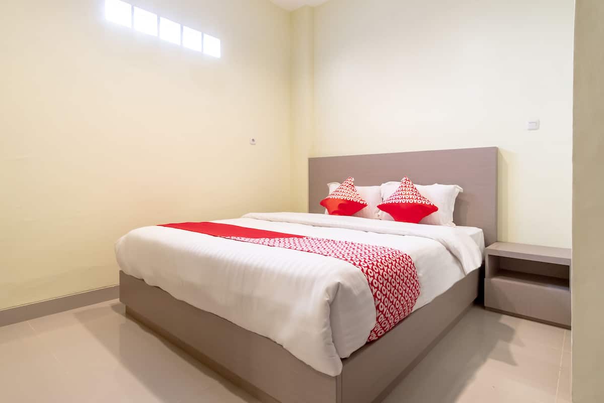 A neatly made bed with a white and red bedspread, two red pillows, and a bedside table with a lamp.