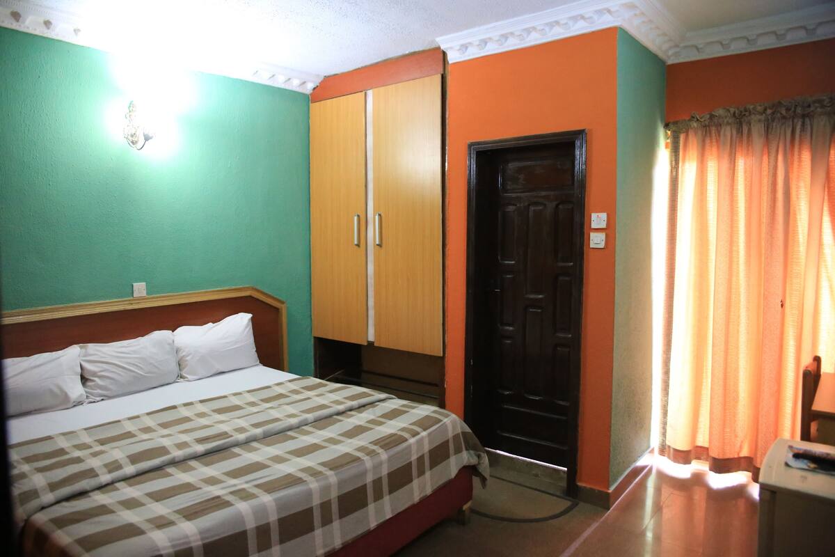 Ein Zimmer mit Bett, Schrank, Tür und Vorhängen.