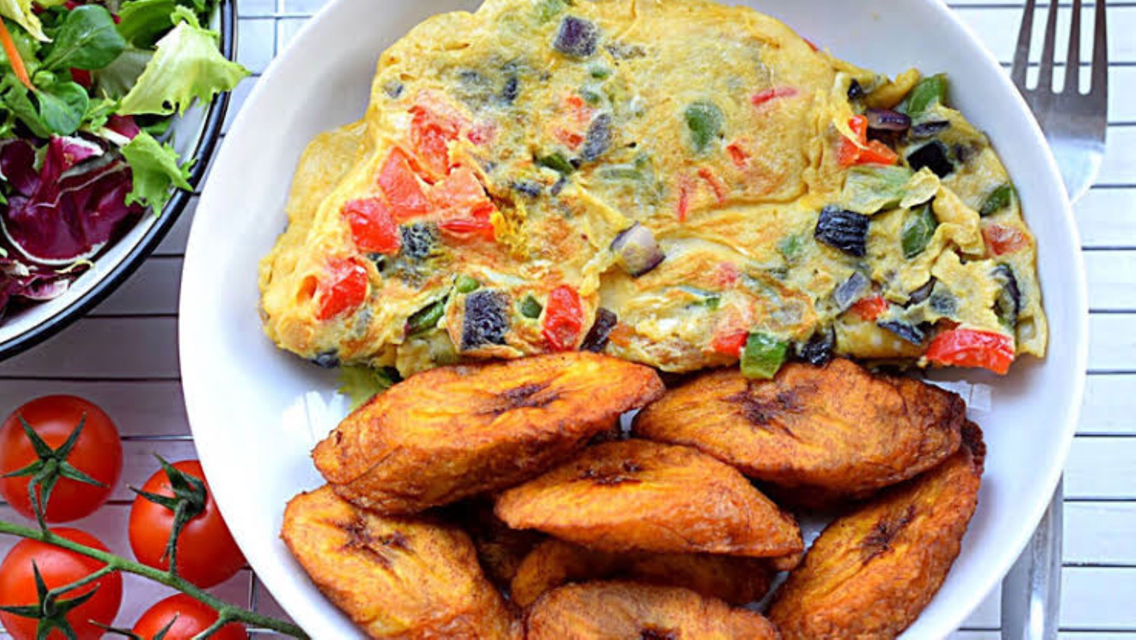 A plate of food with a vegetable omelette and roasted plantains.