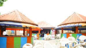 An outdoor seating area with white plastic chairs and tables, covered by striped awnings. - Mokland Hotel and Suites (Lagos)