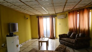 A living room with a sofa, a coffee table, a TV, and a refrigerator. - Mokland Hotel and Suites (Lagos)