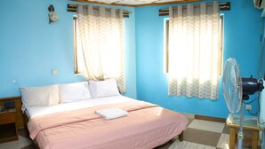 A room with a bed, two windows with curtains, a fan, and a small table. - Mokland Hotel and Suites (Lagos)
