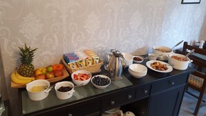 A breakfast buffet with various fruits, cereals, and beverages on a table against a patterned wallpaper background. - Strathmore Guesthouse - Adults Only (Keswick)