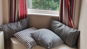 A cozy seating area with a view of a lush green landscape through a window, featuring striped curtains and patterned cushions. - Strathmore Guesthouse - Adults Only (Keswick)
