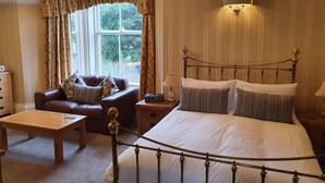 A bedroom with a bed, a wooden nightstand, a leather sofa, a wooden table, and a window with curtains. - Strathmore Guesthouse - Adults Only (Keswick)