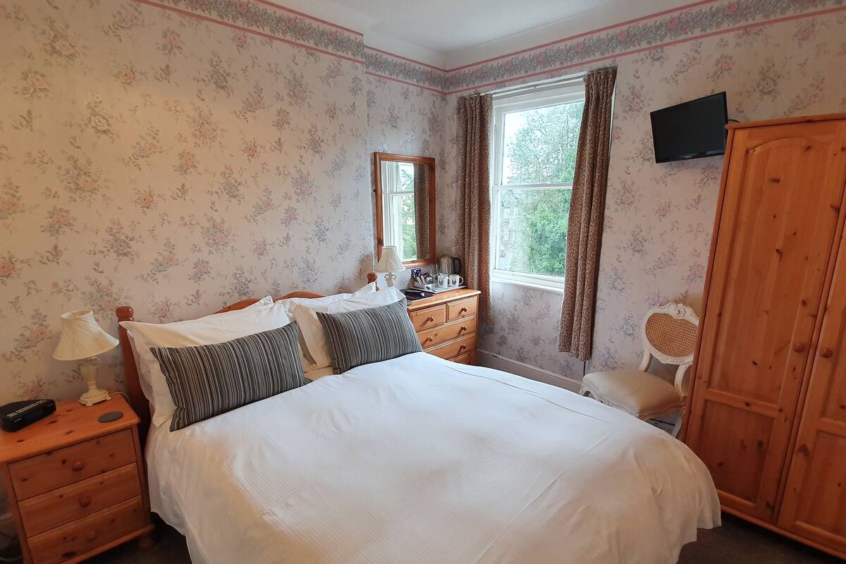 A bedroom with a large bed, wooden nightstand, dresser, and a wardrobe.