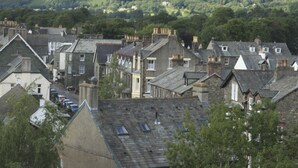 A town with traditional stone buildings, a street with parked cars, and a backdrop of green hills. - Strathmore Guesthouse - Adults Only (Keswick)