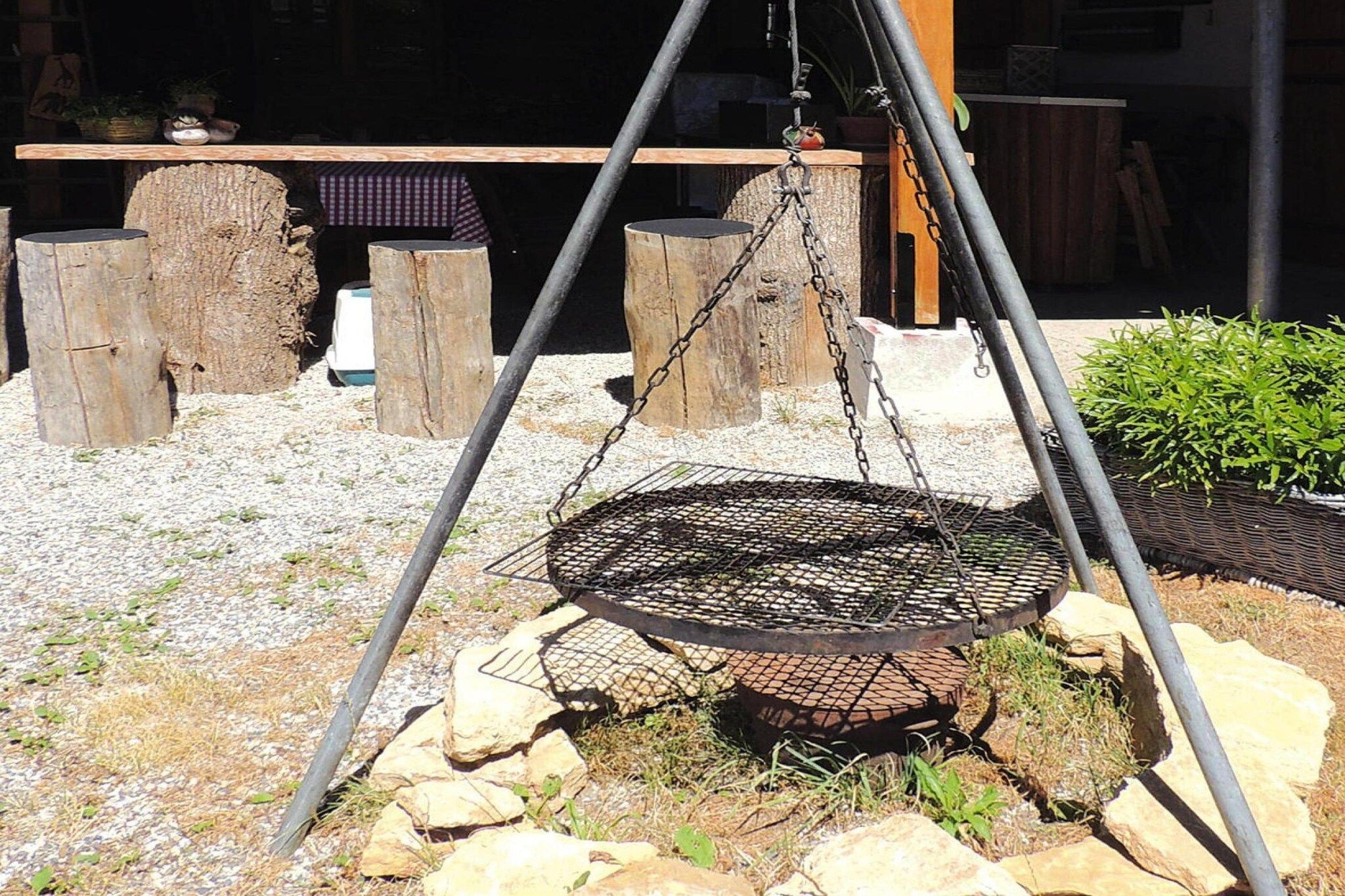 Une chaise suspendue en métal, dotée d’un système de support à chaînes, entourée de rochers et d’une structure en bois.