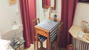 Un pequeño comedor con mantel a cuadros, sillas de madera, una lámpara y un espejo en la pared.