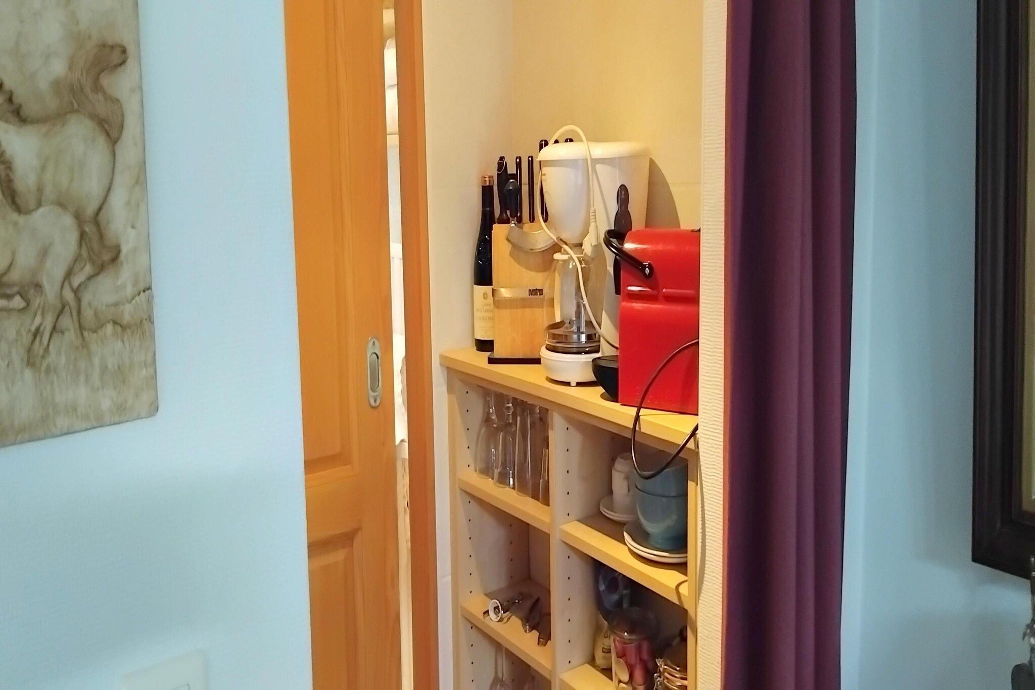 Ett kök med en dörr av trä, en vinflaska, en kaffebryggare och en röd apparat på bänkskivan.