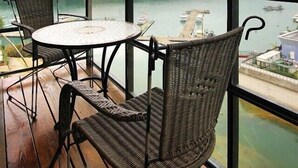 Un balcón con sillas de mimbre y una mesa, con vista a una masa de agua con barcos y un muelle.