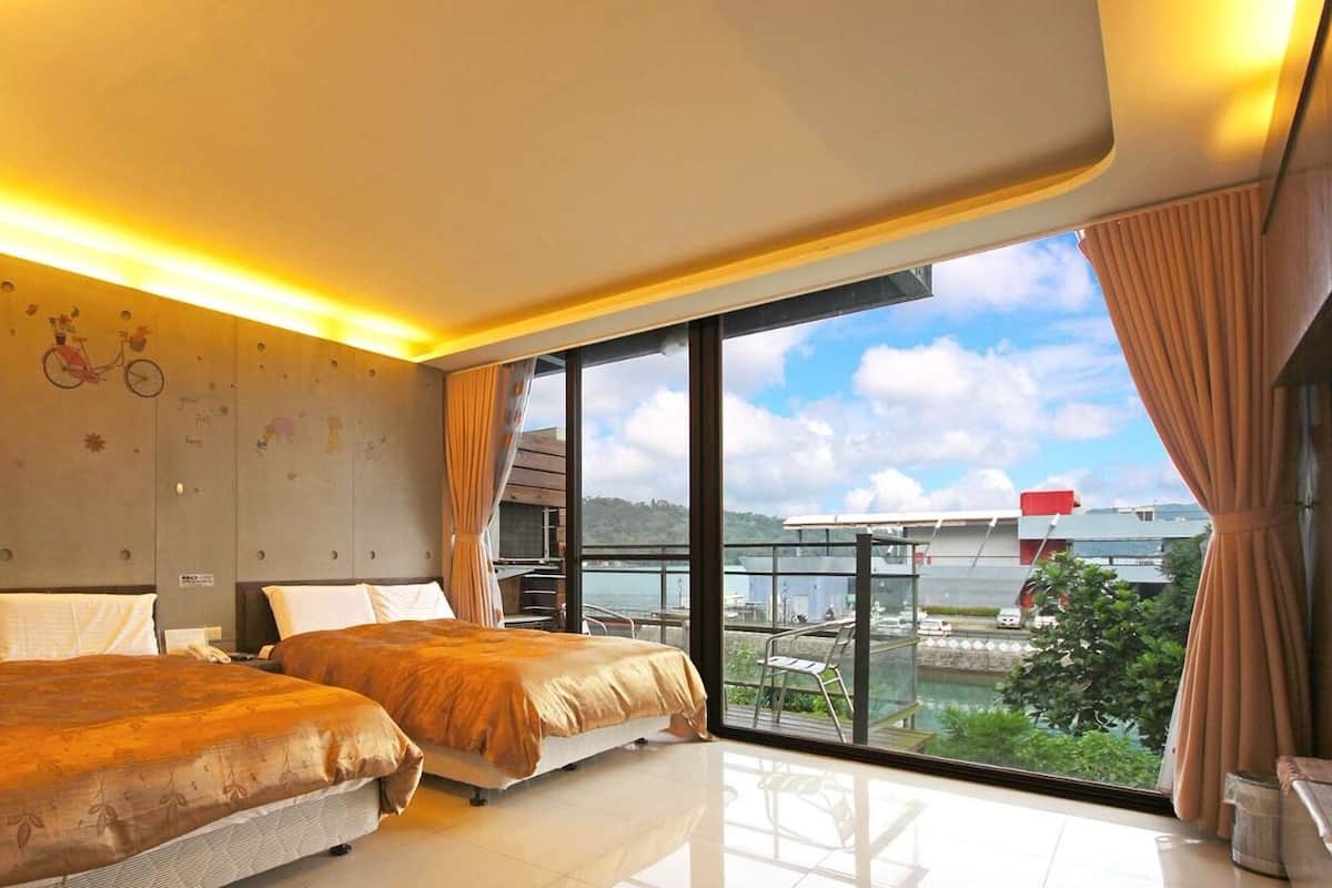 A hotel room with two beds, a large window with a view of the city, and a balcony with a glass railing.