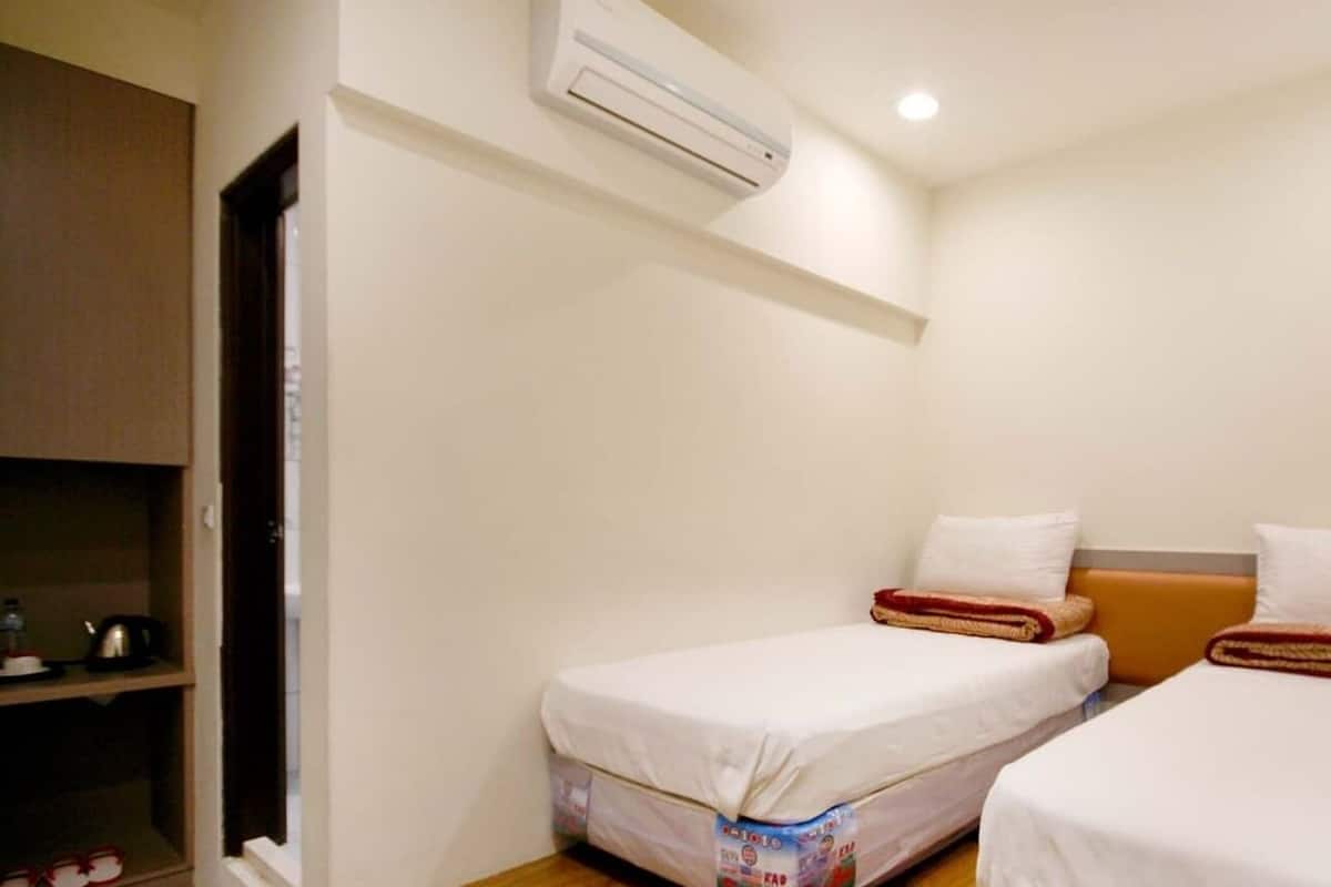 A small, clean room with two single beds, a wardrobe, and an air conditioning unit.