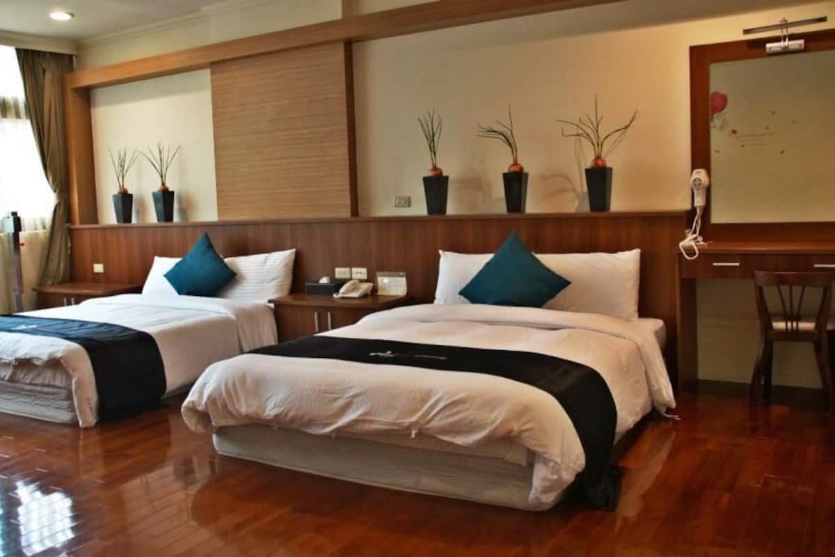 A hotel room with two beds, wooden flooring, a desk, and potted plants.