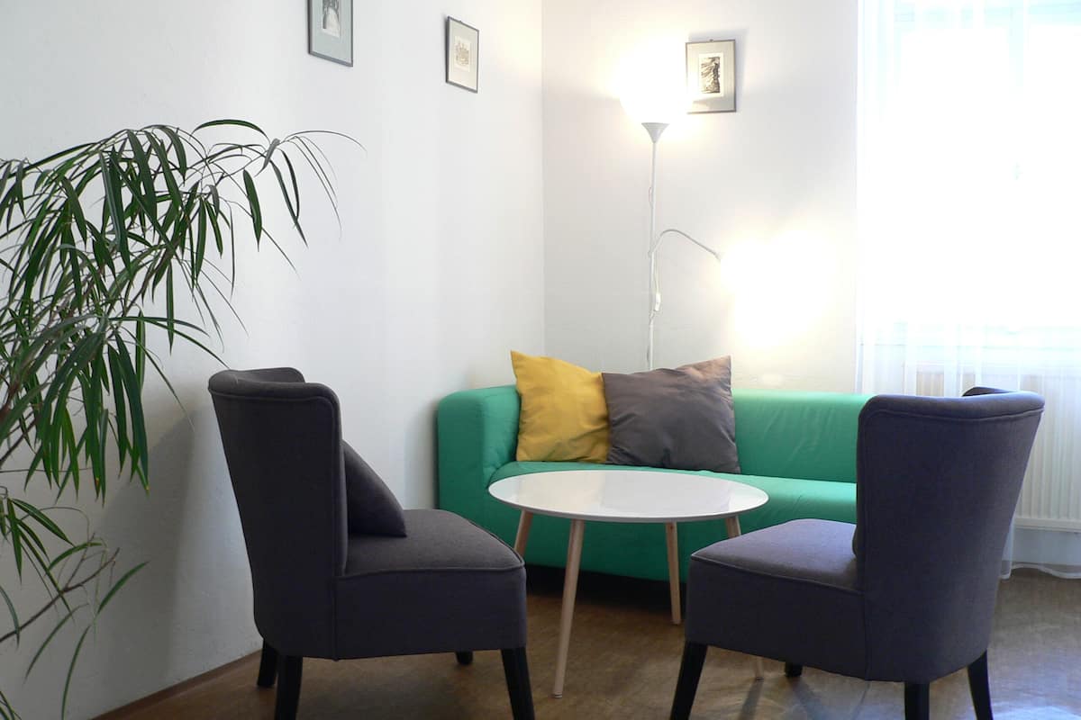 Une pièce comprenant deux chaises, une petite table blanche, un canapé vert avec des coussins et un lampadaire.