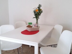 A white table with a red placemat, a wicker basket with a loaf of bread, a vase with flowers, and a green sign. - Teytz Apartments (Prague)