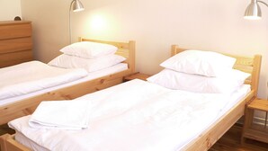 Two single beds with wooden frames and white bedding, a wooden dresser, and two bedside lamps. - Teytz Apartments (Prague)