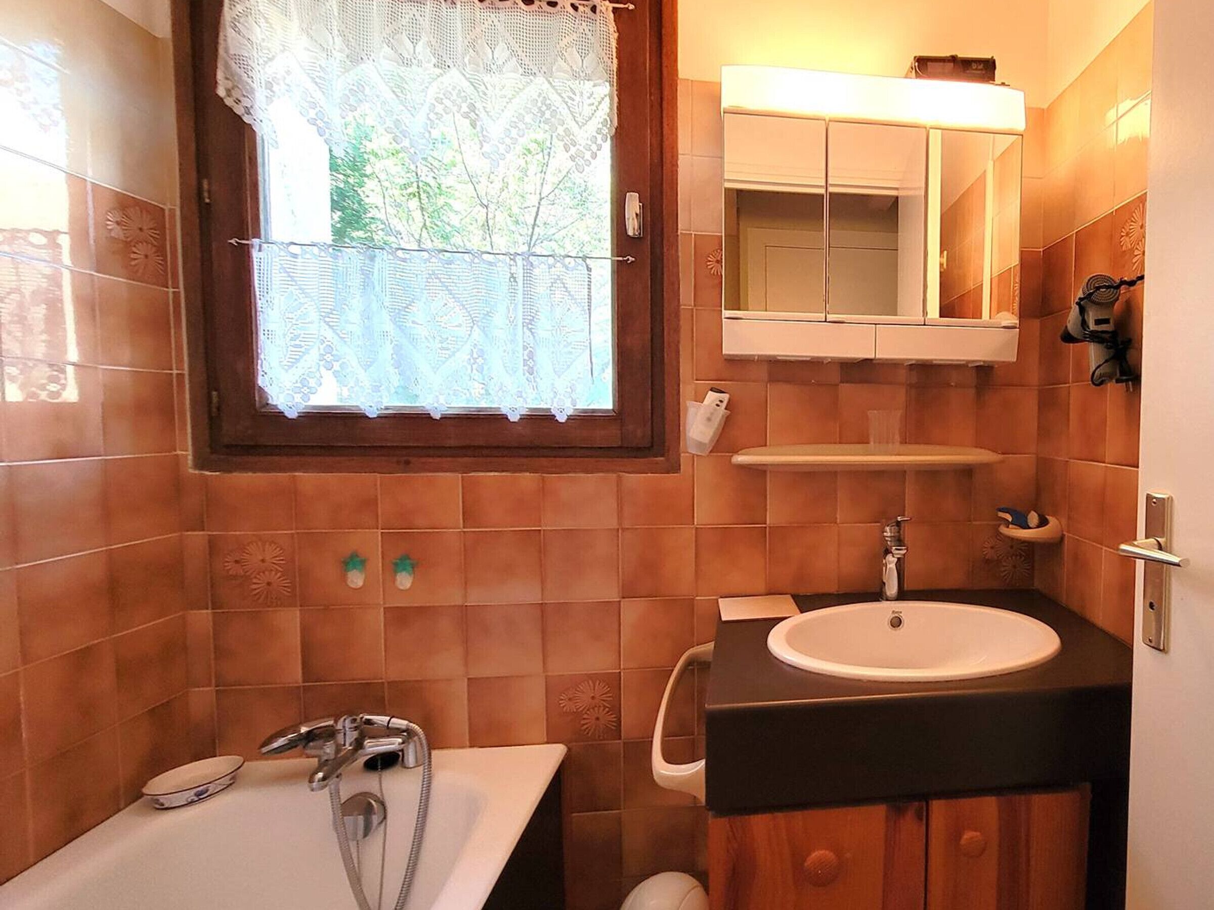 A bathroom with a bathtub, a sink, a mirror, and a window with lace curtains.