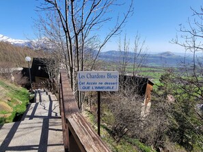 A sign for Les Chardons Bleus with a view of mountains and a wooden pathway.