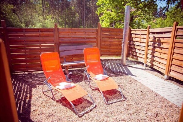Two orange lounge chairs with metal frames and a wooden fence in the background.