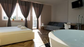 Quarto de hotel com uma cama grande, sofá, mesinha, televisão e banheira.