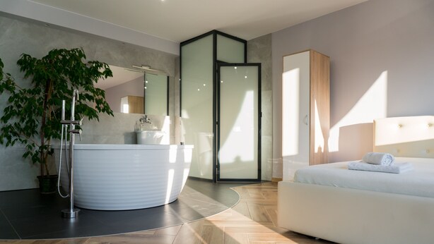 A modern bedroom with a large bed, a built-in bathtub, and a potted plant. - Pensjonat Lubianka (Starachowice)