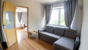 A modern living room with a grey sofa, wooden flooring, a small table, and a window with curtains. - Pensjonat Lubianka (Starachowice)