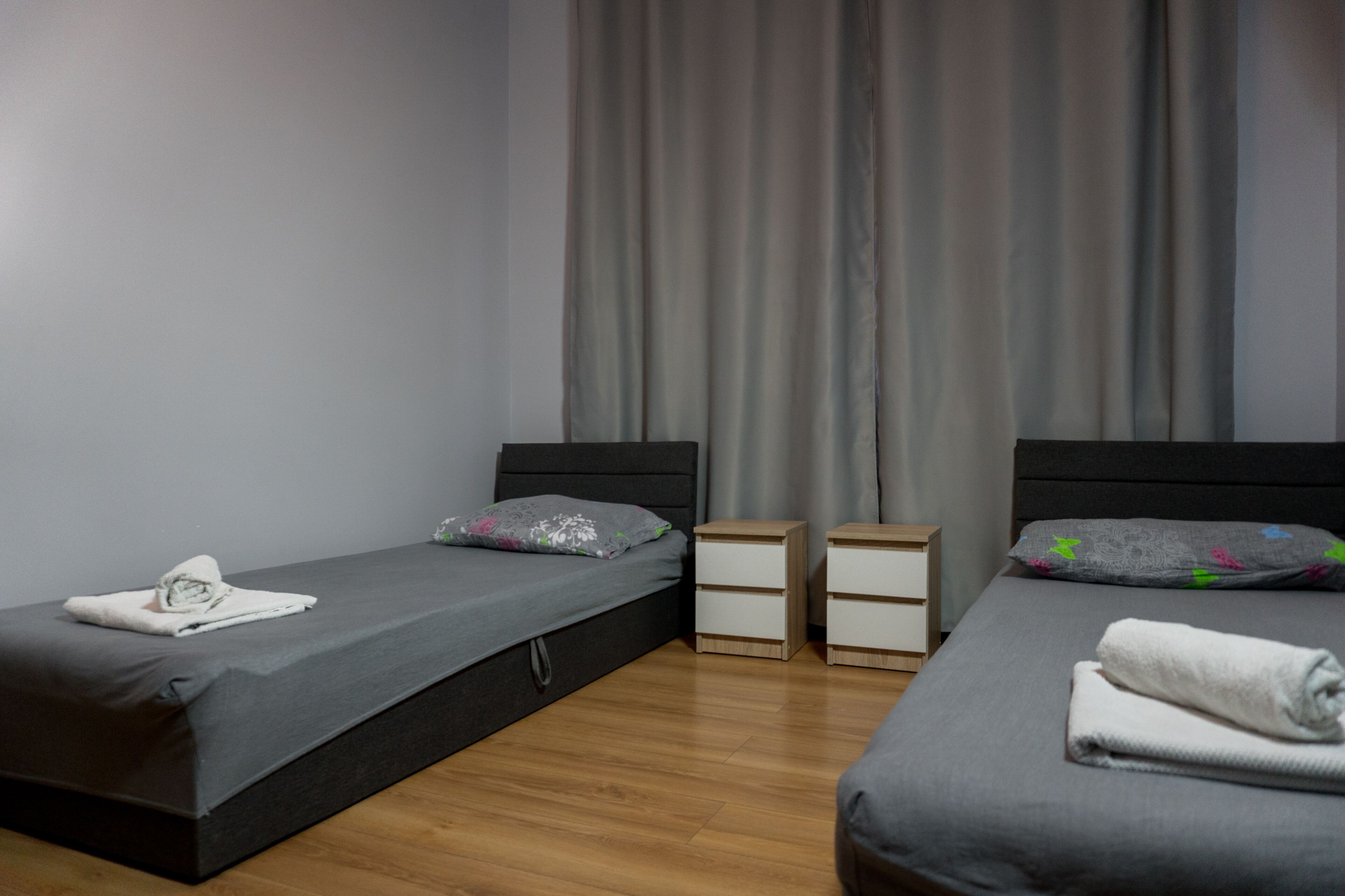 A hotel room with two single beds, each with a pillow and a small bedside table.