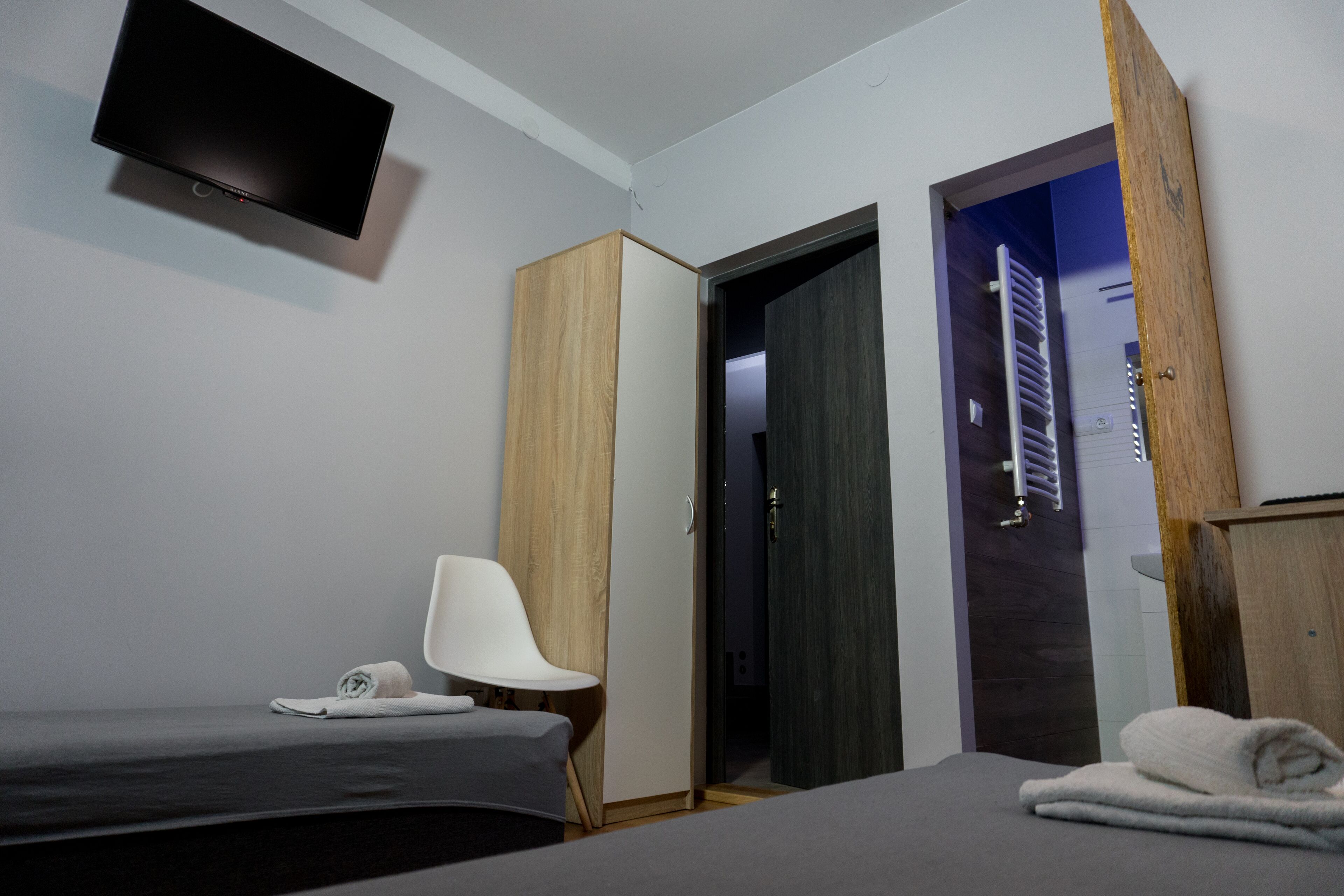 Quarto de hotel com uma cama, uma cadeira, um guarda-roupa e uma televisão na parede.