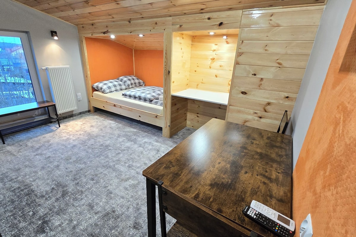 Une petite chambre comprenant un lit, une petite table et une fenêtre donnant sur un paysage enneigé.