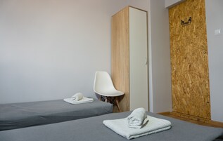 Quarto com duas camas de solteiro, uma cadeira branca e uma porta de madeira com um logotipo.