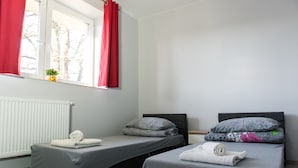 A room with two beds, a window with red curtains, a radiator, and a small plant on the windowsill. - Pensjonat Lubianka (Starachowice)
