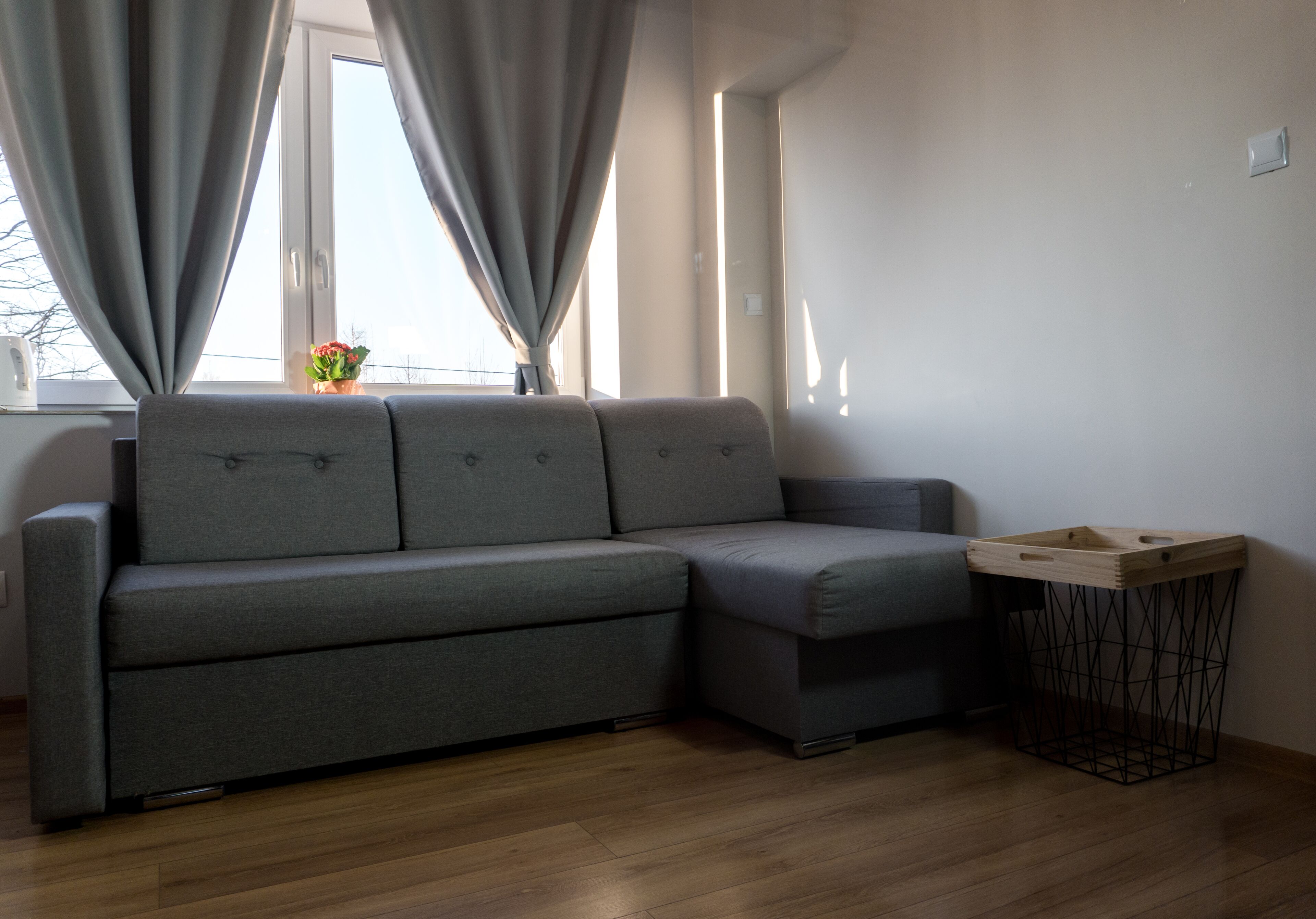 Una sala de estar moderna con un sofá seccional gris, una pequeña mesita de madera y un cubo de basura de metal negro.