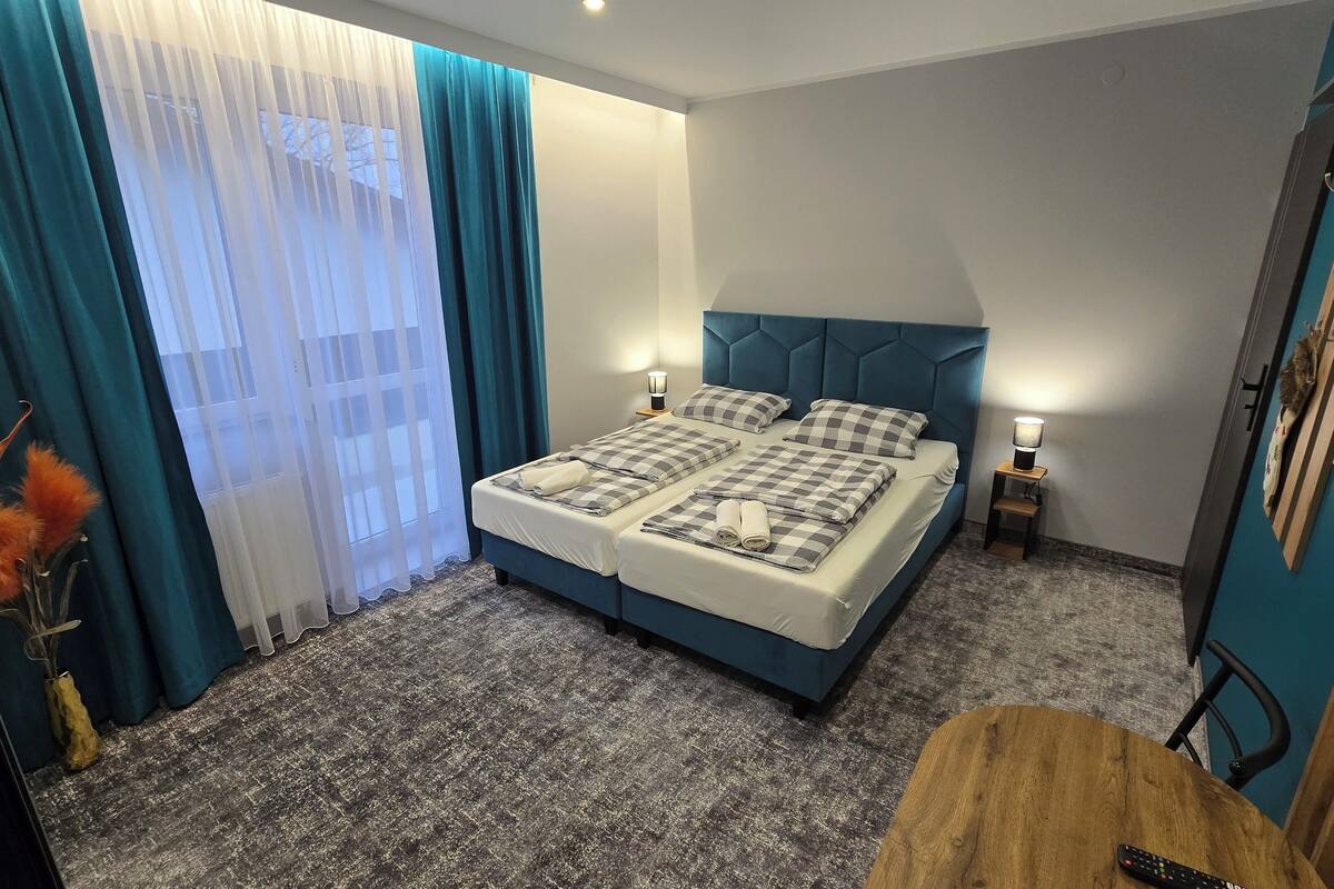 Une chambre à coucher bien rangée, avec un lit, deux tables de chevet dotées de lampes, une petite table en bois et un vase contenant des fleurs oranges.