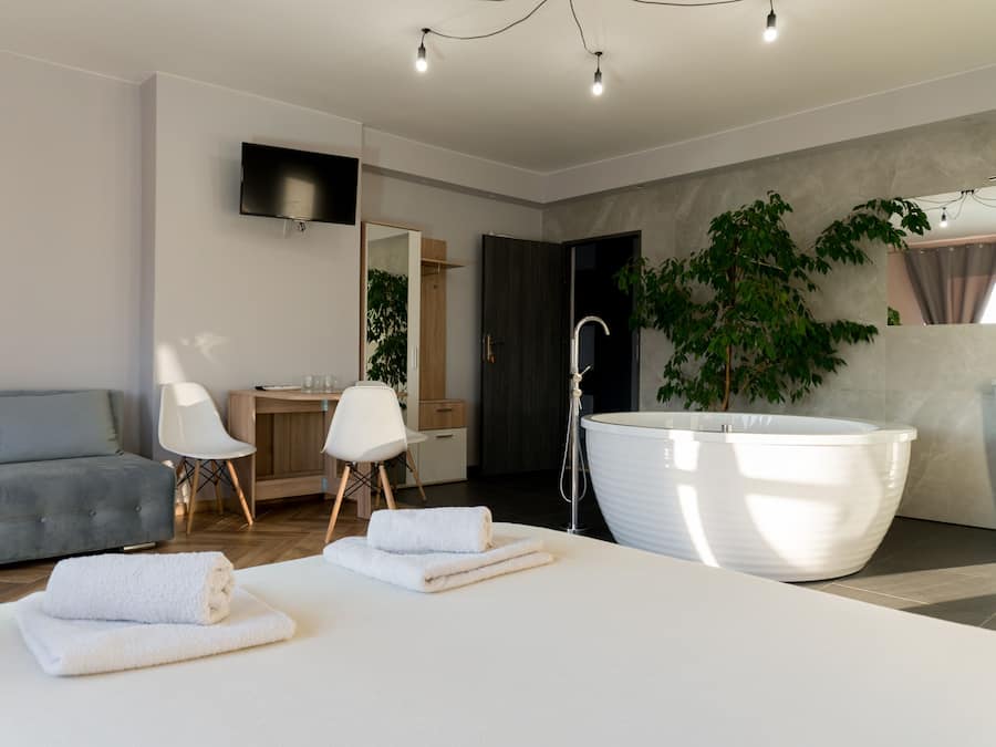 Un baño moderno con una bañera grande, ducha y lavabo. En la zona de estar contigua hay un sofá y una silla.