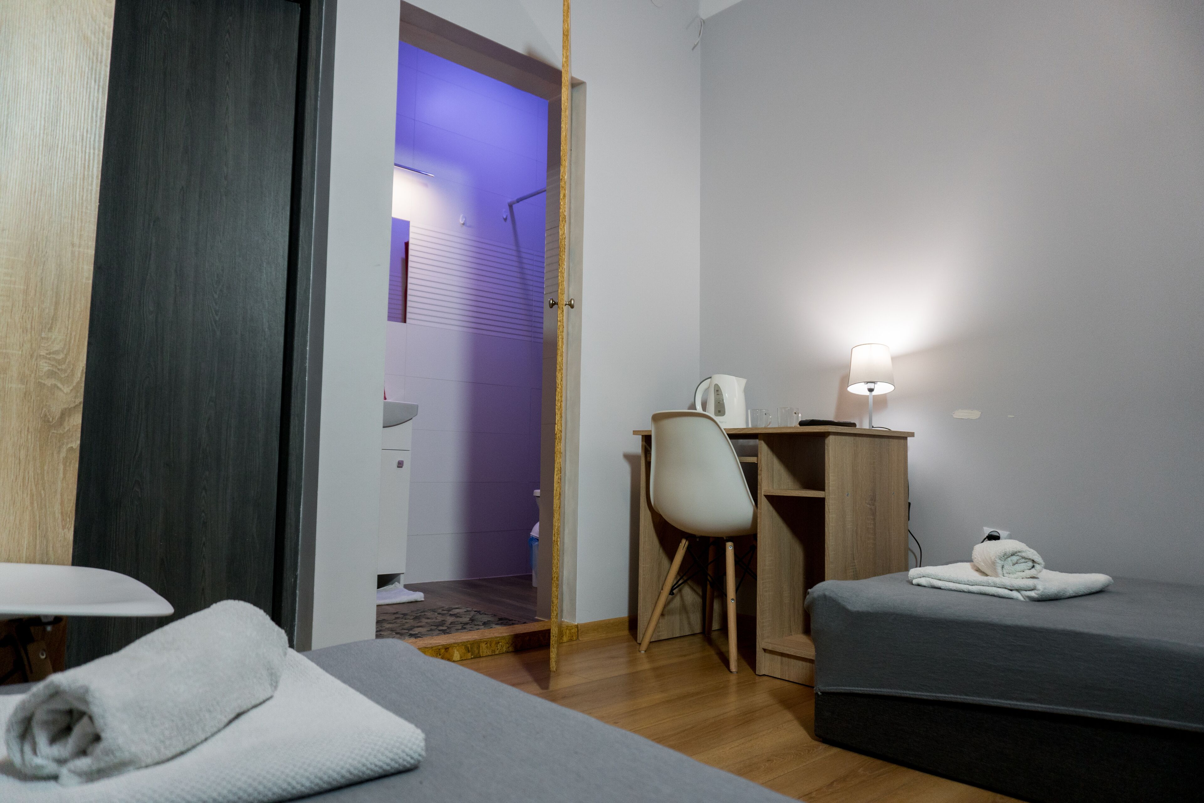 A hotel room with two beds, a desk, a chair, and a lamp.