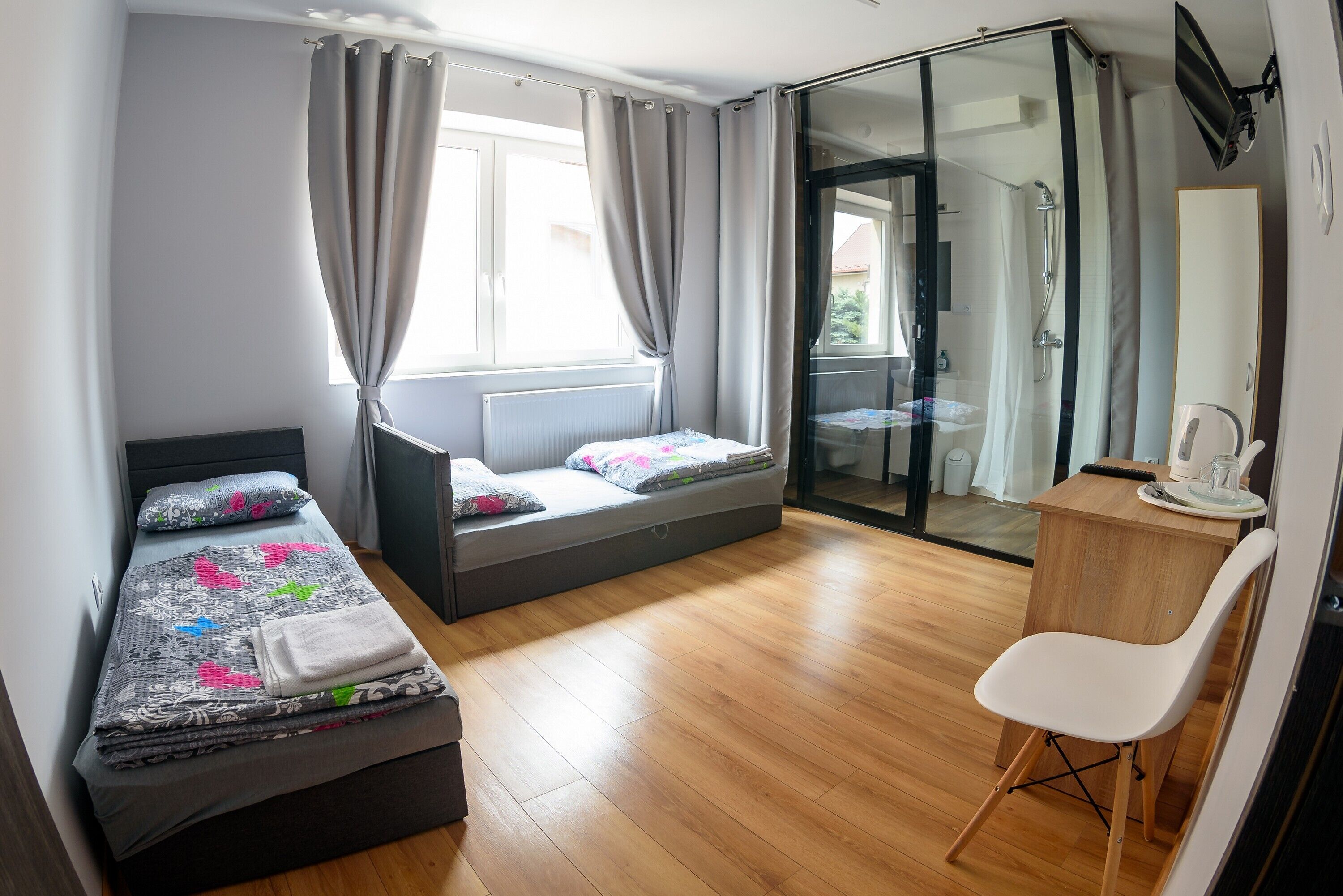 A bedroom with a bed, a desk, and a sliding glass door leading to a shower area.