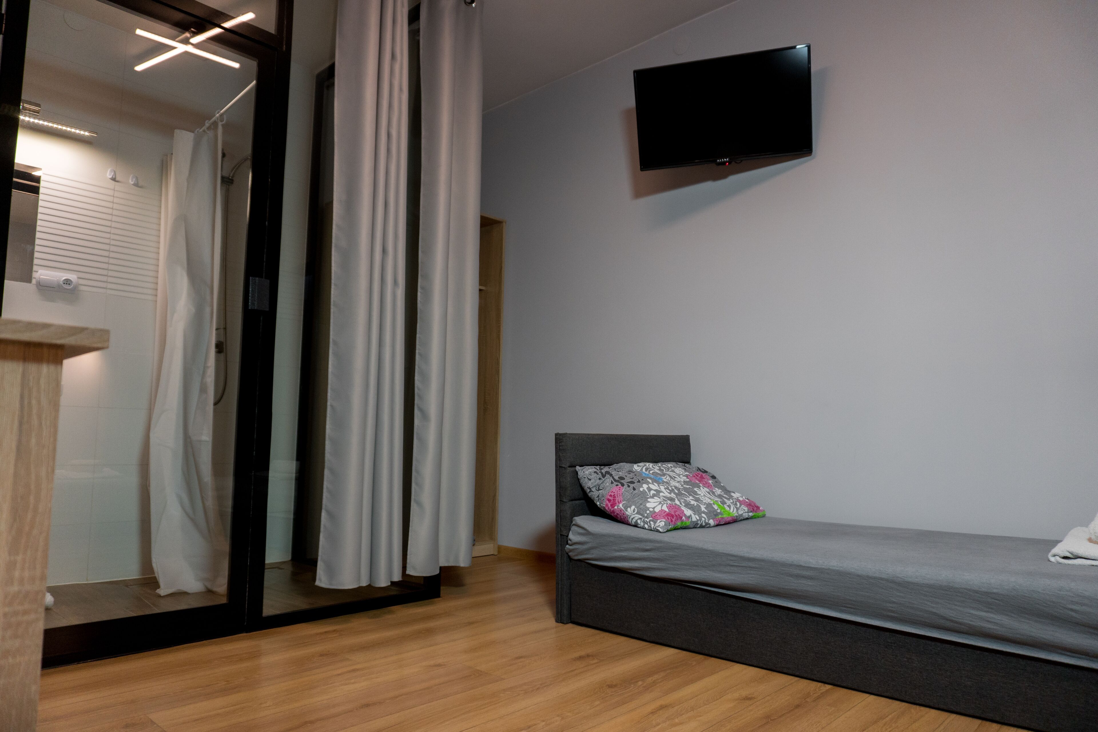 A modern bedroom with a bed, a TV mounted on the wall, and a shower area with curtains.