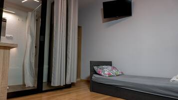 A modern bedroom with a bed, a TV mounted on the wall, and a shower area with curtains.