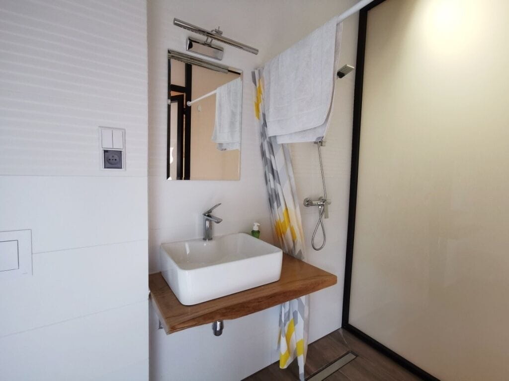 A modern bathroom with a white sink, wooden countertop, and a shower with a towel rack.