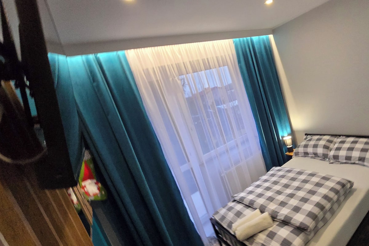 Une petite chambre d’hôtel avec un lit, une table de chevet et une fenêtre avec des rideaux.
