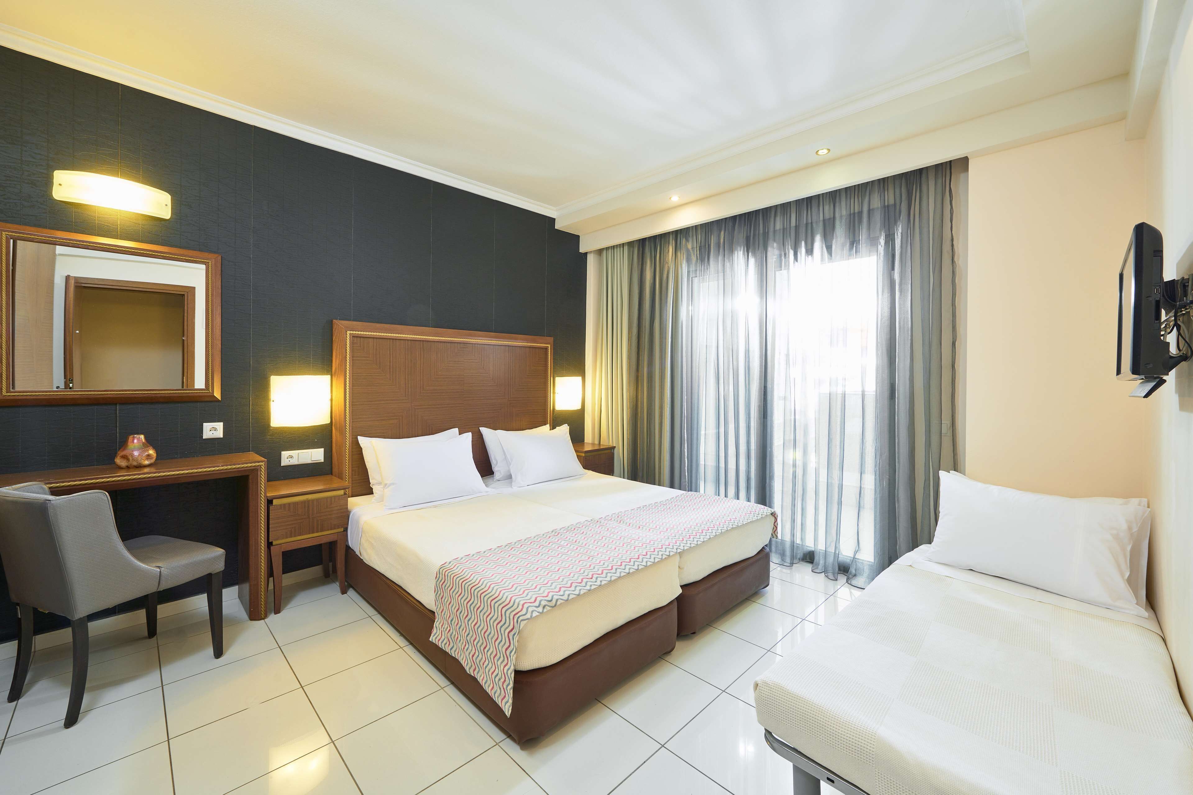A hotel room with a large bed, a desk with a chair, a TV, and a mirror.