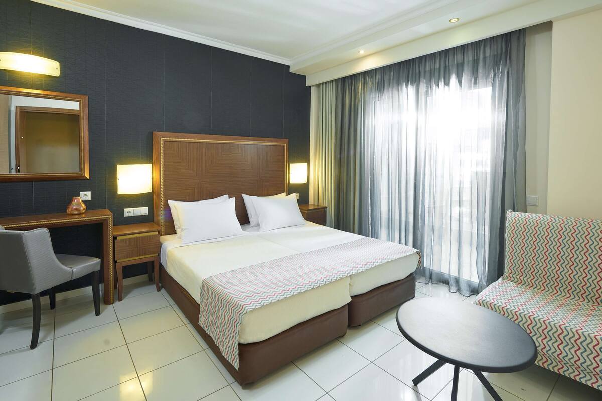 A hotel room with a bed, a desk, a chair, a sofa, and a small table.