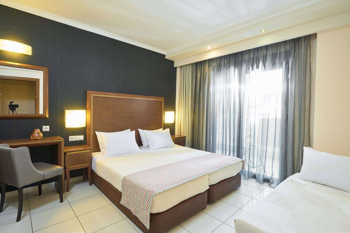 A hotel room with a large bed, a desk, a chair, a mirror, and a window with curtains.