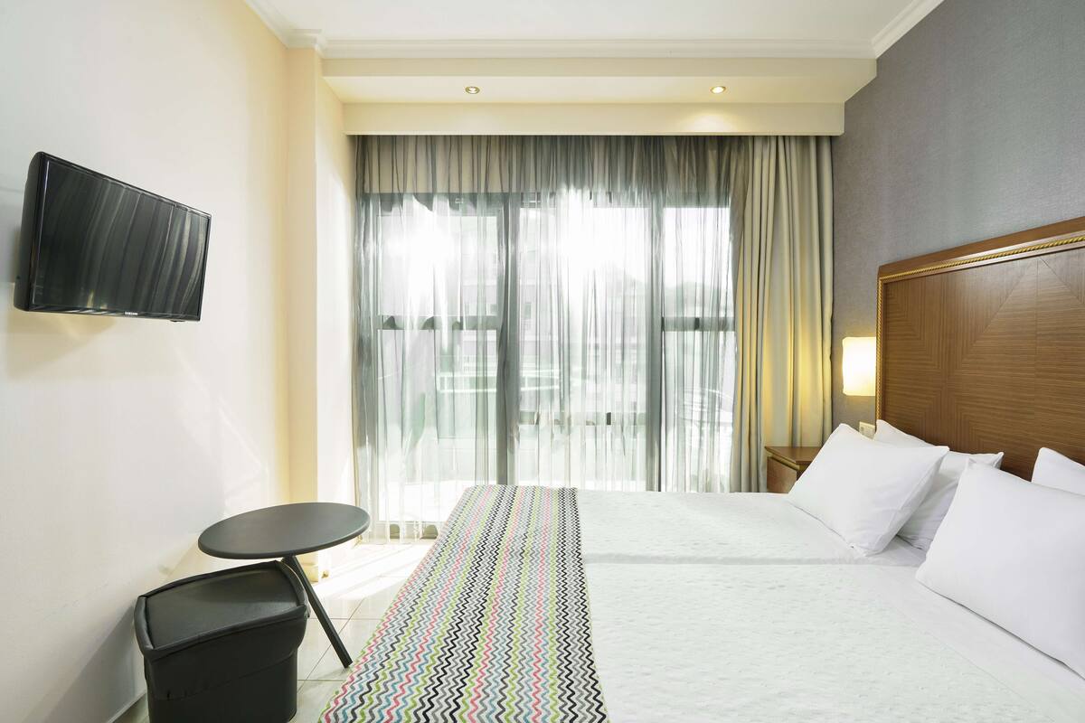 A hotel room with a bed, a TV mounted on the wall, a small table, and a trash bin.