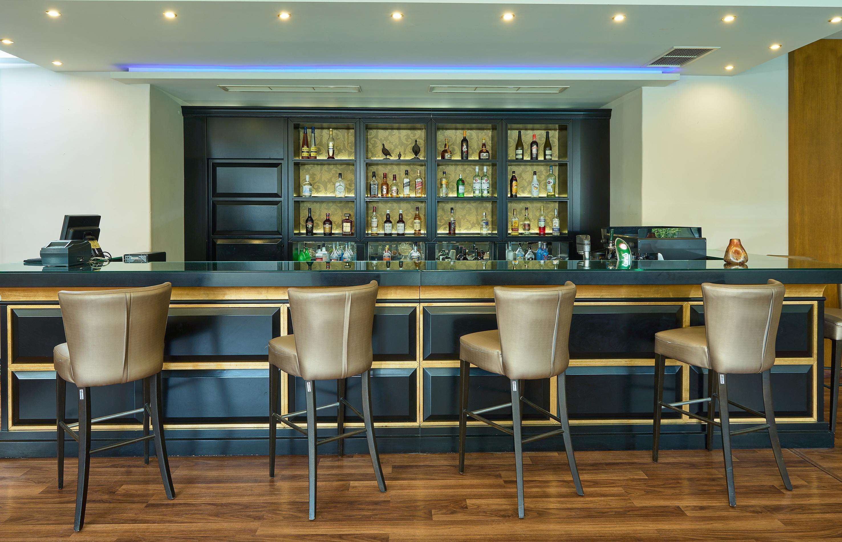 A bar area with a counter, multiple shelves of bottles, and four bar stools.