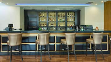 A bar area with a counter, multiple shelves of bottles, and four bar stools.